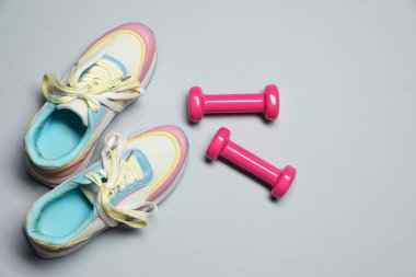Dumbbells and sneakers on light grey background, flat lay. Space for text