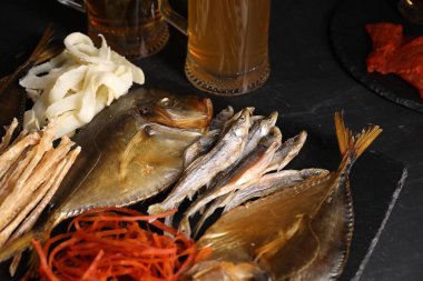 Different dried fish snacks and beer on black table, closeup
