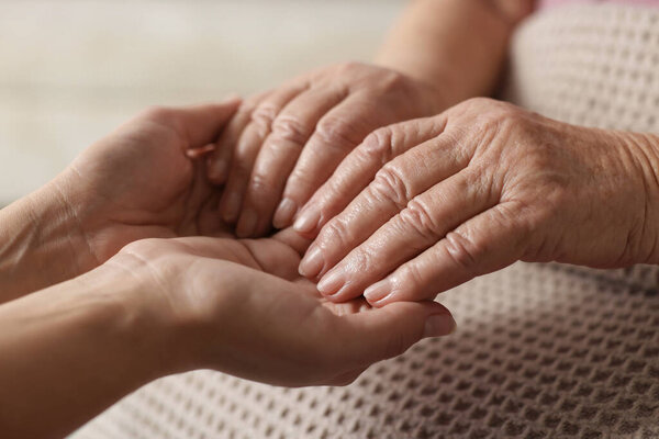 Caregiver supporting senior woman on light background, closeup. Elderly care