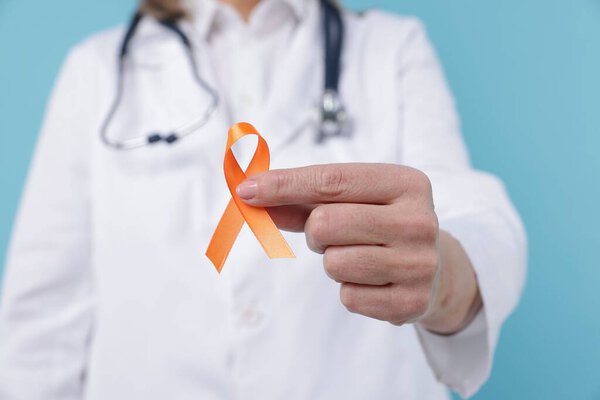 Multiple Sclerosis awareness. Doctor with orange ribbon on light blue background, closeup