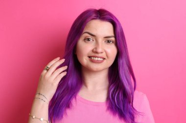 Pembe arka planda parlak mor saçlı ve dövmeli güzel bir kadın.