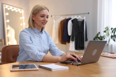 İşyeri sahibi, terzi dükkanındaki masada dizüstü bilgisayarla çalışıyor.
