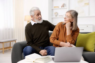 Sevimli yaşlı çift evdeki kanepede birbirlerine bakıyor.