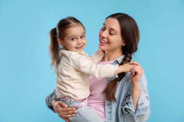 Açık mavi arka planda sevimli kızıyla mutlu anne portresi.