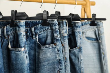 Many stylish jeans hanging from rack on white background, closeup