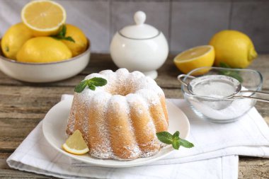 Pudra şekerli lezzetli limonlu pasta, taze meyve dilimi ve ahşap masada nane.