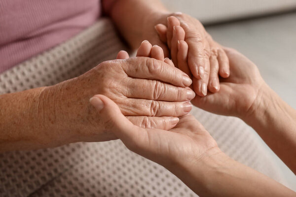 Caregiver supporting senior woman on light background, closeup. Elderly care