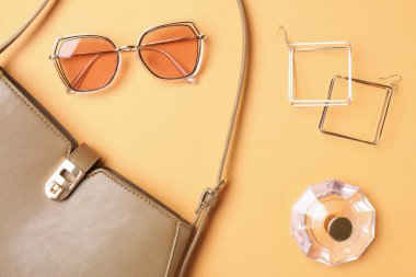 Beautiful bag, perfume and stylish accessories on pale orange background, flat lay