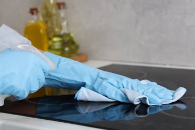 Temizlik ürünü kullanan bir kadın, indüksiyon tenceresini paçavrayla temizlerken, yakın plan
