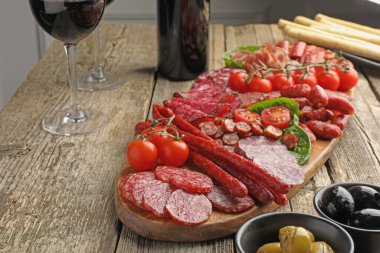 Farklı tütsülenmiş sosisler ve ahşap masada sunulan diğer aperatifler.