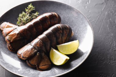 Çiğ ıstakoz kuyruğu, kireç ve kekik siyah masada, yakın plan.