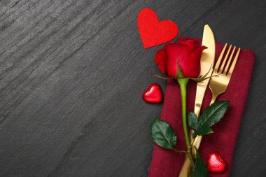 Siyah masa üzerinde kırmızı gül ve çatal bıçak seti olan romantik bir yer. Sevgililer Günü kutlaması