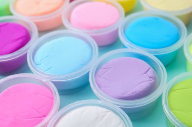 Açık mavi arka planda plastik kavanozlardaki farklı renkli modelleme killeri, yakın plan