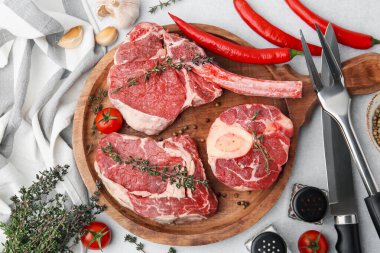 Çiğ et, baharat, ürün ve çatal bıçak parçaları açık gri masada, düz yerde.