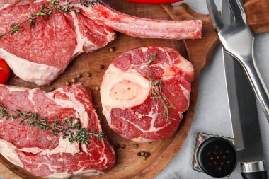 Çiğ et, baharat ve çatal bıçak parçaları açık gri masada, düz yerde.