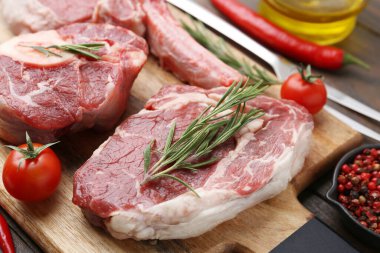 Ahşap masada çiğ et, baharat ve domates parçaları, yakın plan.