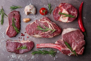 Flat lay composition with pieces of raw beef, salt, rosemary and products on brown textured table
