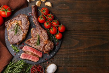 Pieces of delicious beef meat, spices and tomatoes on wooden table, flat lay. Space for text