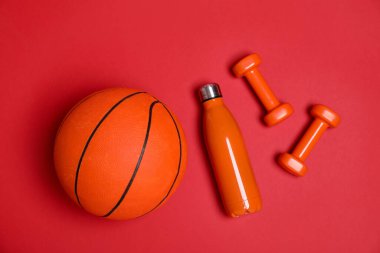 Dambıllar, su şişesi ve kırmızı arka planda basketbol topu, düz konum. Spor malzemeleri.