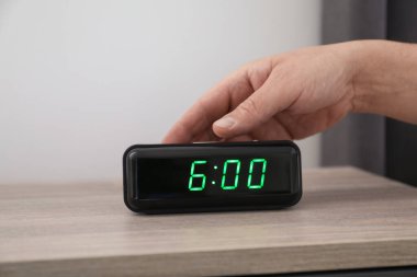 Kapalı bir odada, komodinin üzerindeki dijital çalar saati kapatan adam.