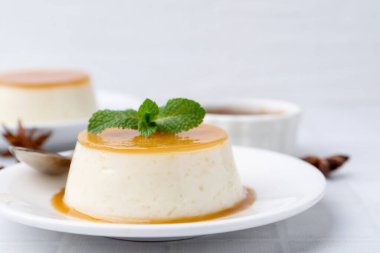 Beyaz fayanslı masada servis edilen karamelli puding, yakın plan.
