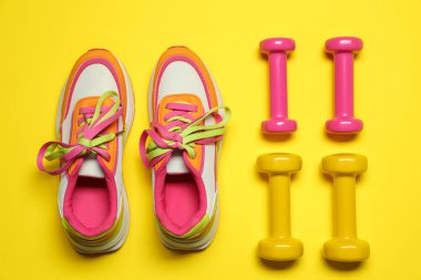 Sarı arka planda dambıllar ve spor ayakkabılar, düz yatış