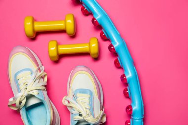 Dambıllar, spor ayakkabılar ve parlak pembe arka planda hula hoop, düz uzanma