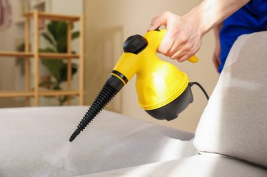 Temizlikçi kanepeyi evde buharlı temizleme makinesiyle temizliyor.