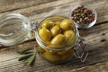 Cam kavanozda turşulu yeşil zeytin ve ahşap masada baharatlar, yakın plan.