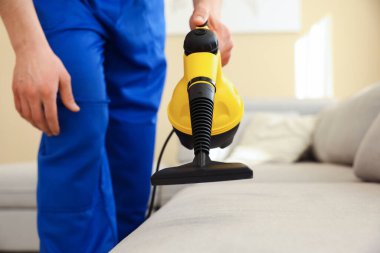 Temizlikçi kanepeyi evde buharlı temizleme makinesiyle temizliyor.