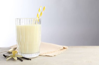 Bir bardak süt, vanilya kapsülü, çiçek ve kaşık açık gri masada, metin için boşluk