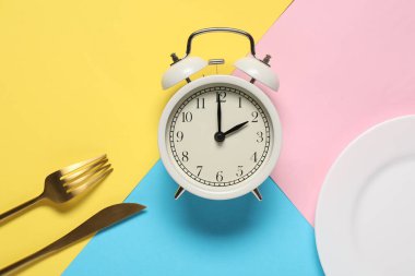 Yemek zamanı. Alarm saati, tabak ve çatal bıçak takımı renk arkaplanında, düz konum