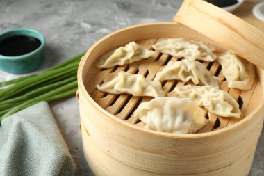 Bambu buharlı tencerede kaynamış gyoza (hamur tatlısı), açık gri masada, yakın plan.