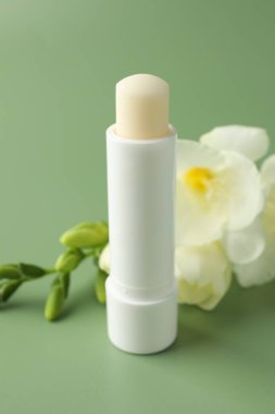 Açık yeşil arka planda dudak kremi ve frezya çiçekleri, yakın plan.