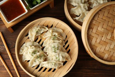 Bambu buharlı buharda kaynamış gyoza (hamur tatlısı), sos ve çubuklar ahşap masada, düz yerde.