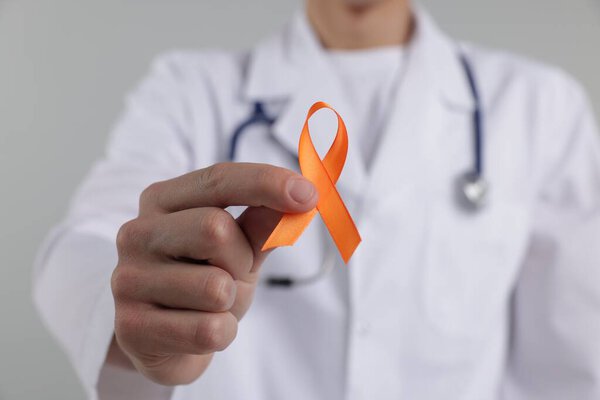 Multiple Sclerosis awareness. Doctor with orange ribbon on light grey background, closeup