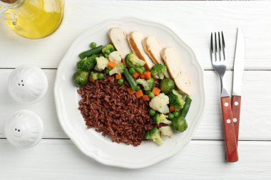 Lezzetli kahverengi pirinç, sebzeli ve tavuklu beyaz ahşap masada servis ediliyor.