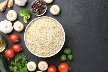 Tabaktaki çiğ kahverengi pirinç taze ürünlerin arasında koyu dokulu masada, düz yerde. Metin için boşluk