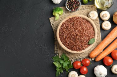 Tabaktaki çiğ kahverengi pirinç taze ürünlerin arasında koyu dokulu masada, düz yerde. Metin için boşluk