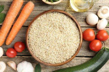 Tabaktaki çiğ kahverengi pirinç taze ürünlerin arasında, ahşap masada, düz yerde.