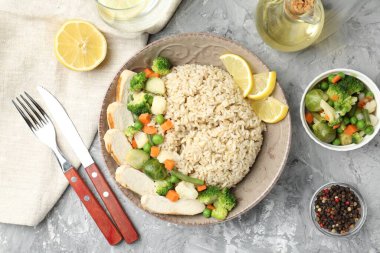 Gri desenli masada servis edilen tavuk, sebze ve limon dilimli lezzetli kahverengi pirinç.