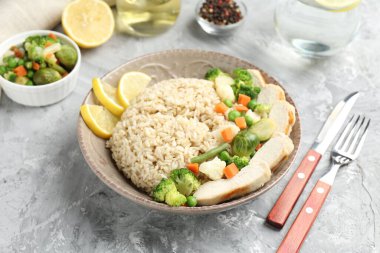 Gri desenli masada servis edilen tavuk, sebze ve limon dilimleri ile nefis kahverengi pirinç, yakın plan.