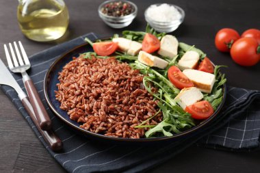 Lezzetli kahverengi pirinç, tavuk, roka ve domatesler siyah ahşap masada, yakın plan.