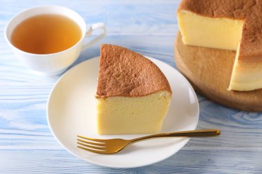 Tasty Japanese Castella sponge cake, tea and fork on light blue wooden table, closeup