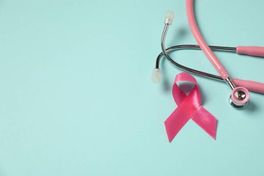 Göğüs kanseri farkındalığı. Açık mavi arka planda pembe kurdele ve steteskop. Metin için boşluk