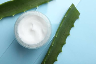 Açık mavi zemin üzerinde krema ve aloe yaprakları, düz yatıyordu