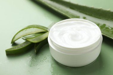 Aloe vera özütüyle nemlendirici krem, yeşil arkaplanda yapraklar ve su damlaları, yakın plan