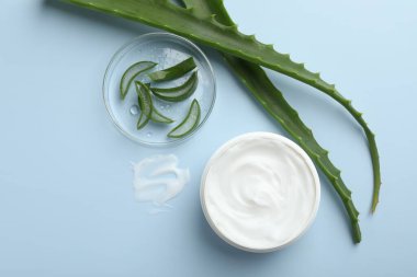 Aloe vera özütüyle nemlendirici krem ve açık mavi arkaplanda yapraklar, düz bir zemin.