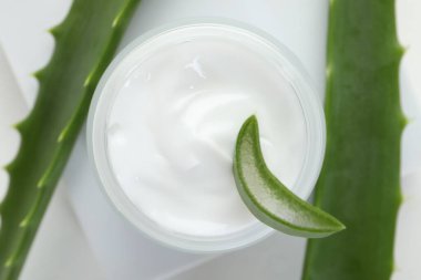 Aloe vera özütüyle nemlendirici krem ve beyaz arkaplanda yapraklar, düz bir zemin.