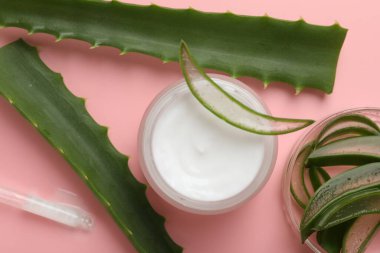 Kavanozda aloe vera özütüyle nemlendirici krem ve pembe arka planda yapraklar.
